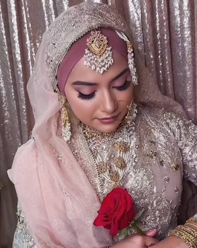 Bride in a blush pink hijab and embellished outfit holding a red rose